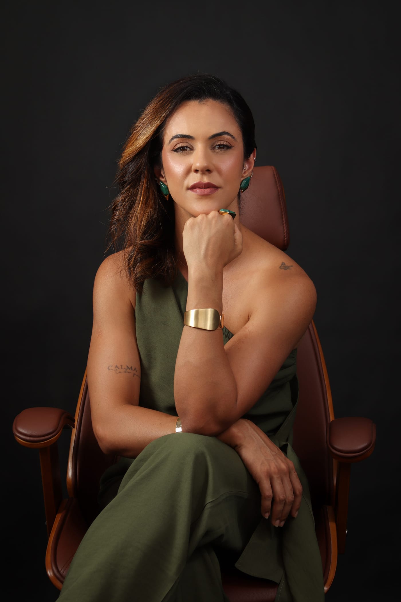 Retrato de Ana Paula Rodrigues sentada em poltrona de couro, vestindo macacão verde